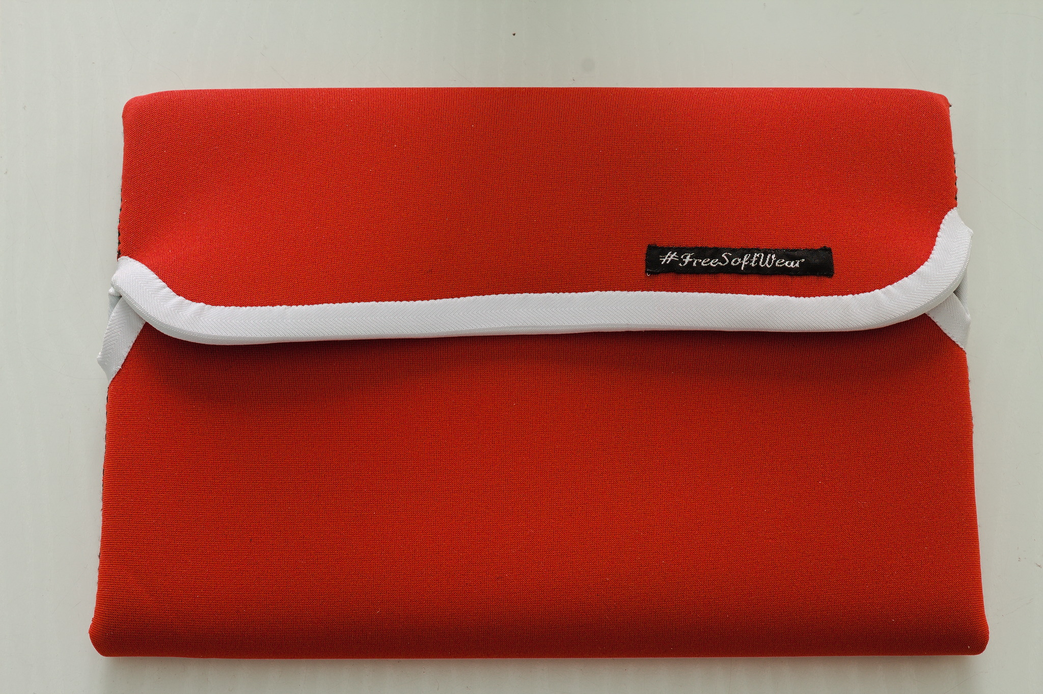 Picture of a red neoprene laptop sleeve, with two overlapping flaps with rounded edges for closure.