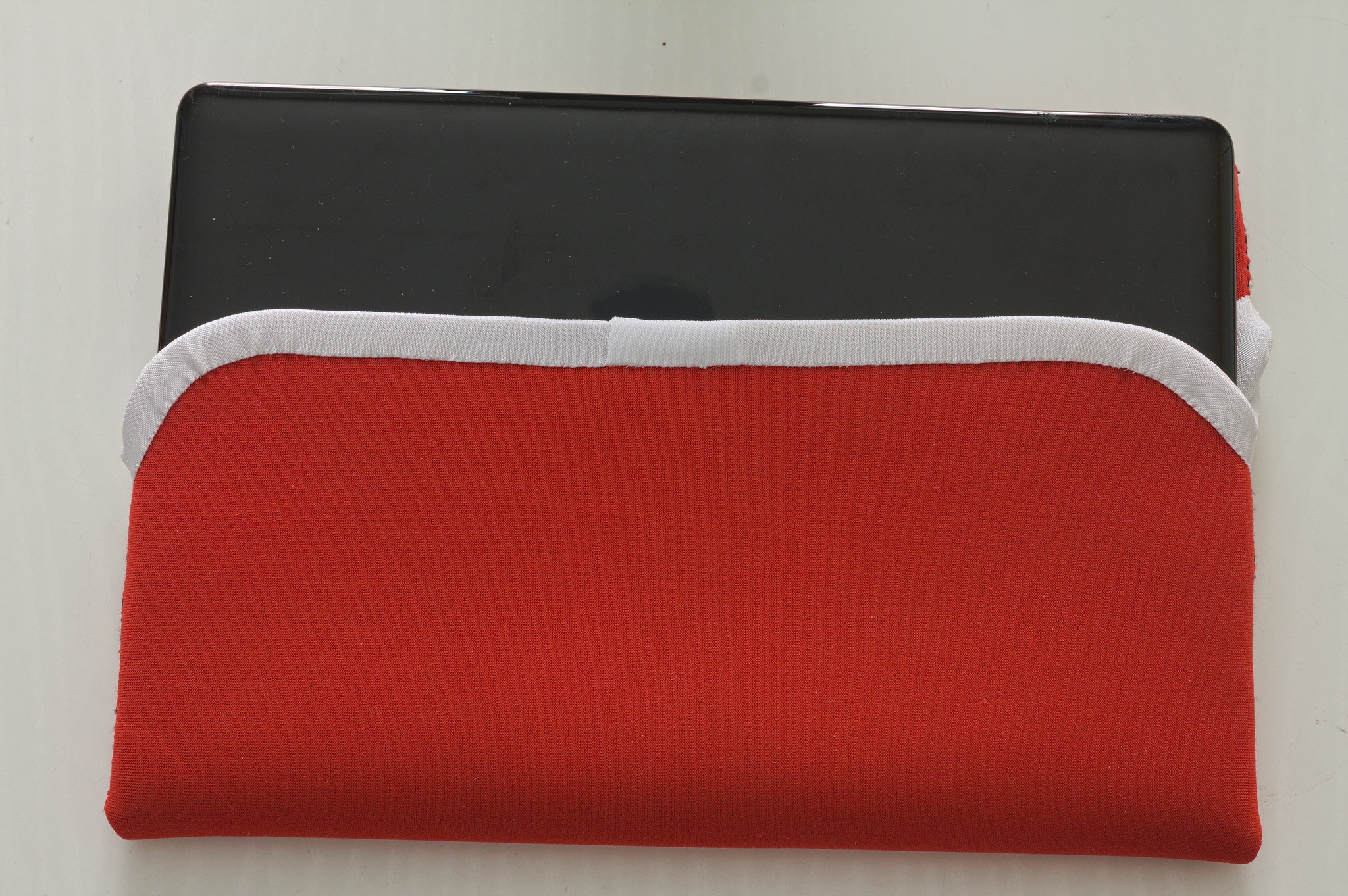 Picture of a red neoprene laptop sleeve, partially open with a laptop visible inside.