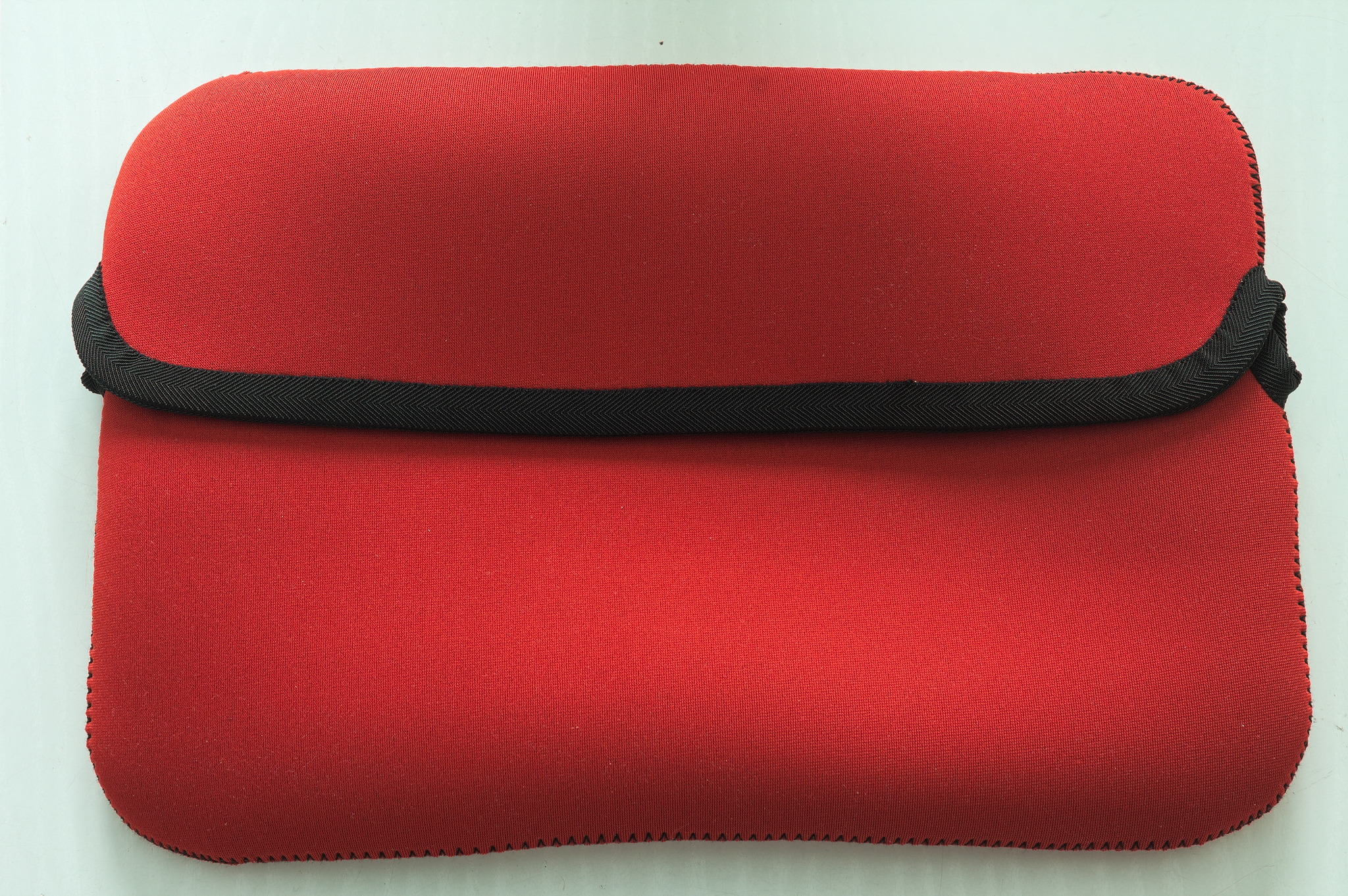 Picture of a red neoprene laptop sleeve, with rounder corners and currently empty.
